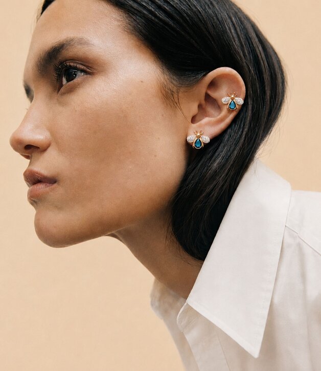 A woman wearing a dark grey herringbone wool blazer with a set of yellow gold, diamond-embellished necklace, rings, ear cuff and bangle