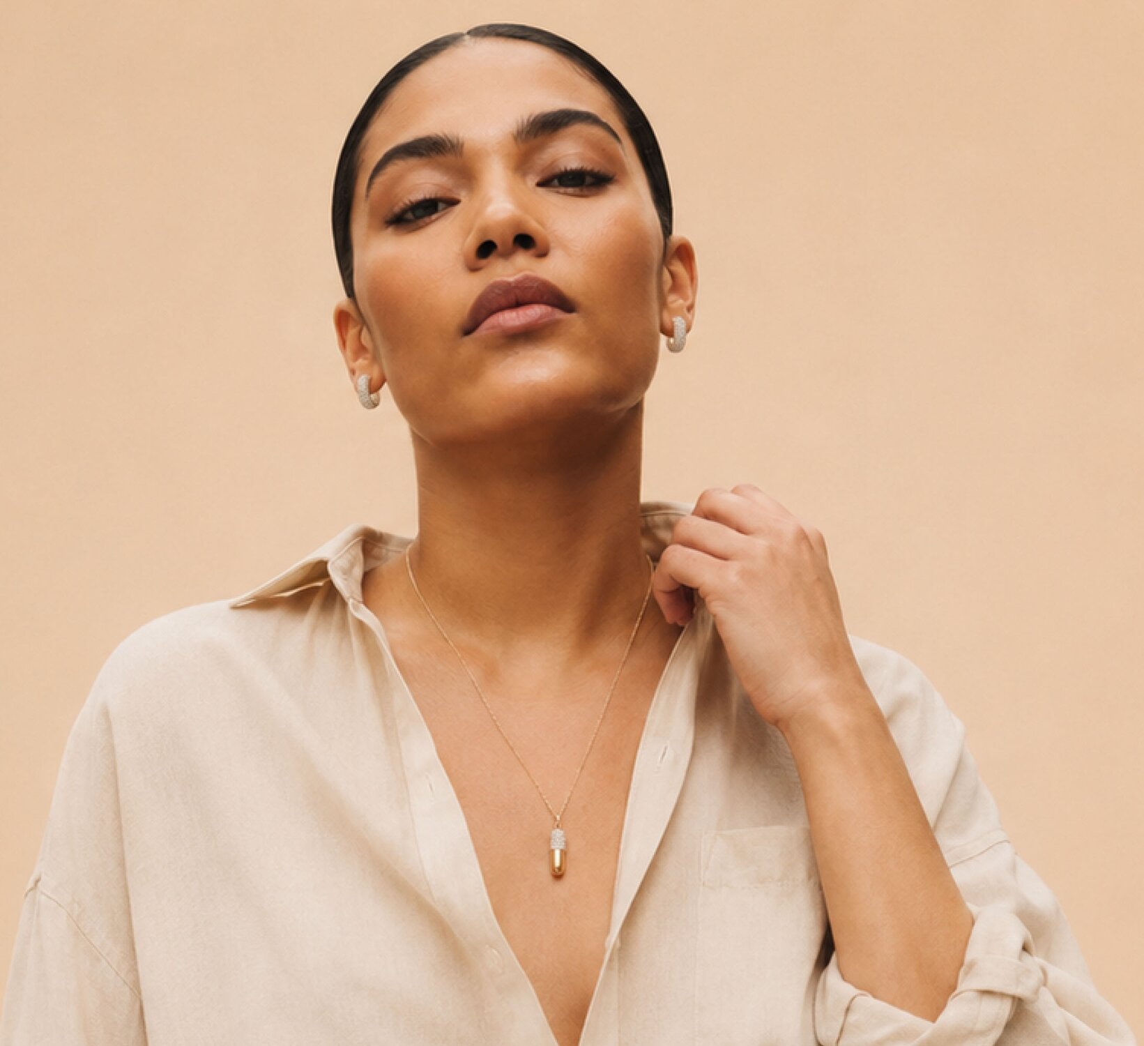 A woman wearing a dark grey herringbone wool blazer with a set of yellow gold, diamond-embellished necklace, rings, ear cuff and bangle