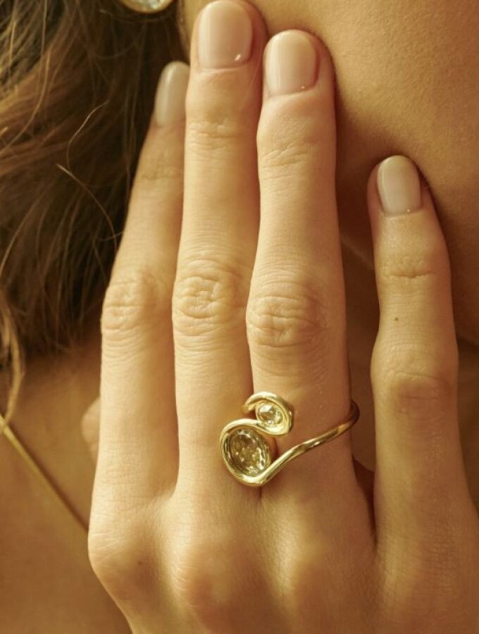 A person wearing a yellow gold sculptural, curved ring featuring loose diamonds encased inside a bezel