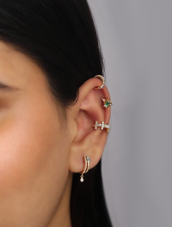 A person wearing four yellow gold diamond and gem-embellished earrings on one ear