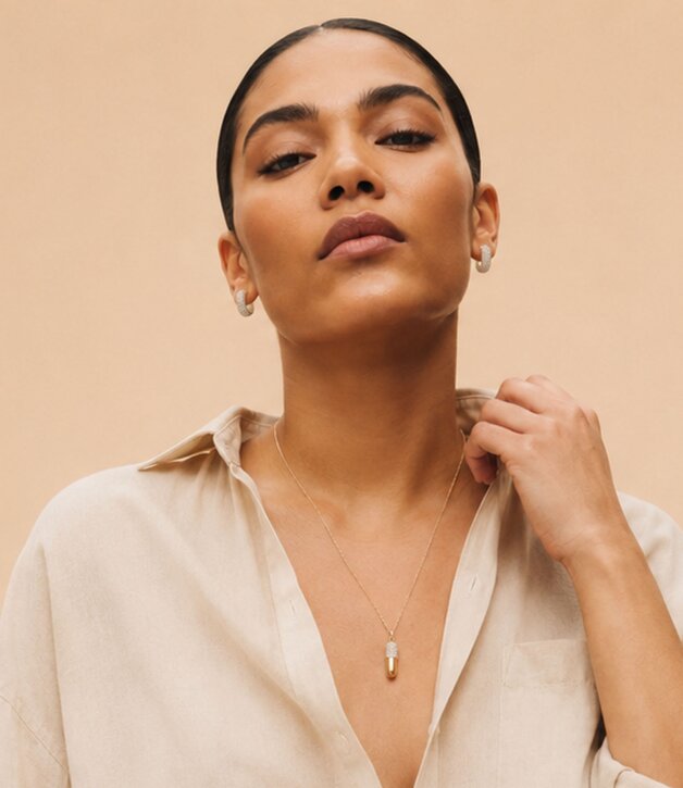 A woman wearing a dark grey herringbone wool blazer with a set of yellow gold, diamond-embellished necklace, rings, ear cuff and bangle