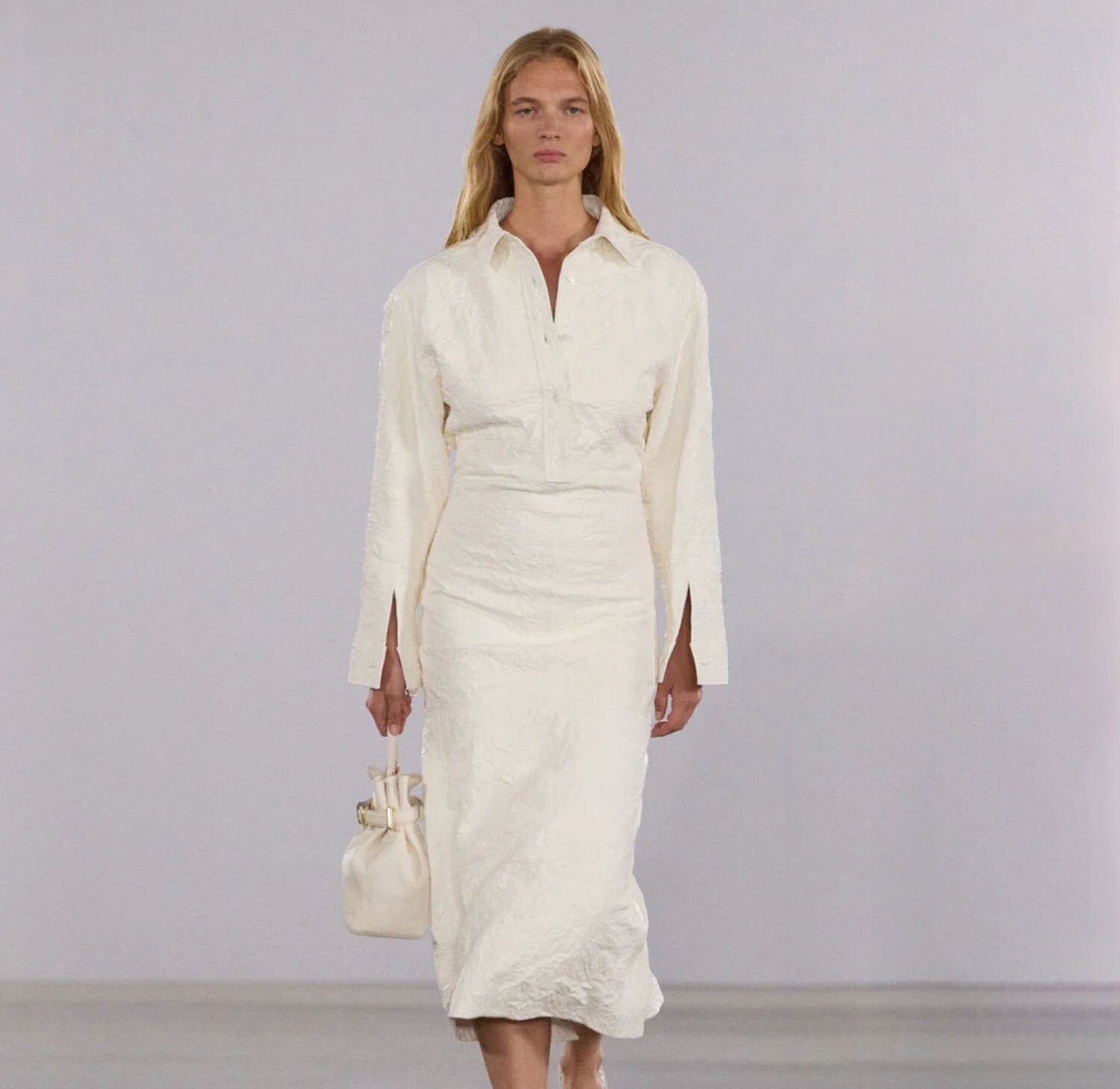 A woman wearing an ecru button-up long-sleeve top and column midi skirt