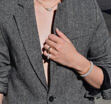 A woman wearing a dark grey herringbone wool blazer with a set of yellow gold, diamond-embellished necklace, rings, ear cuff and bangle