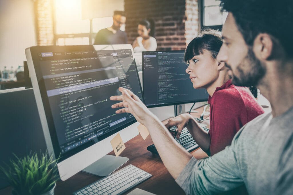 A male and female colleague looking at code on a computer screen