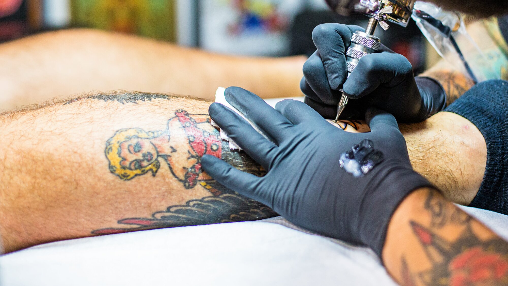 Tattoo artist works on a large piece of art on a man's leg 