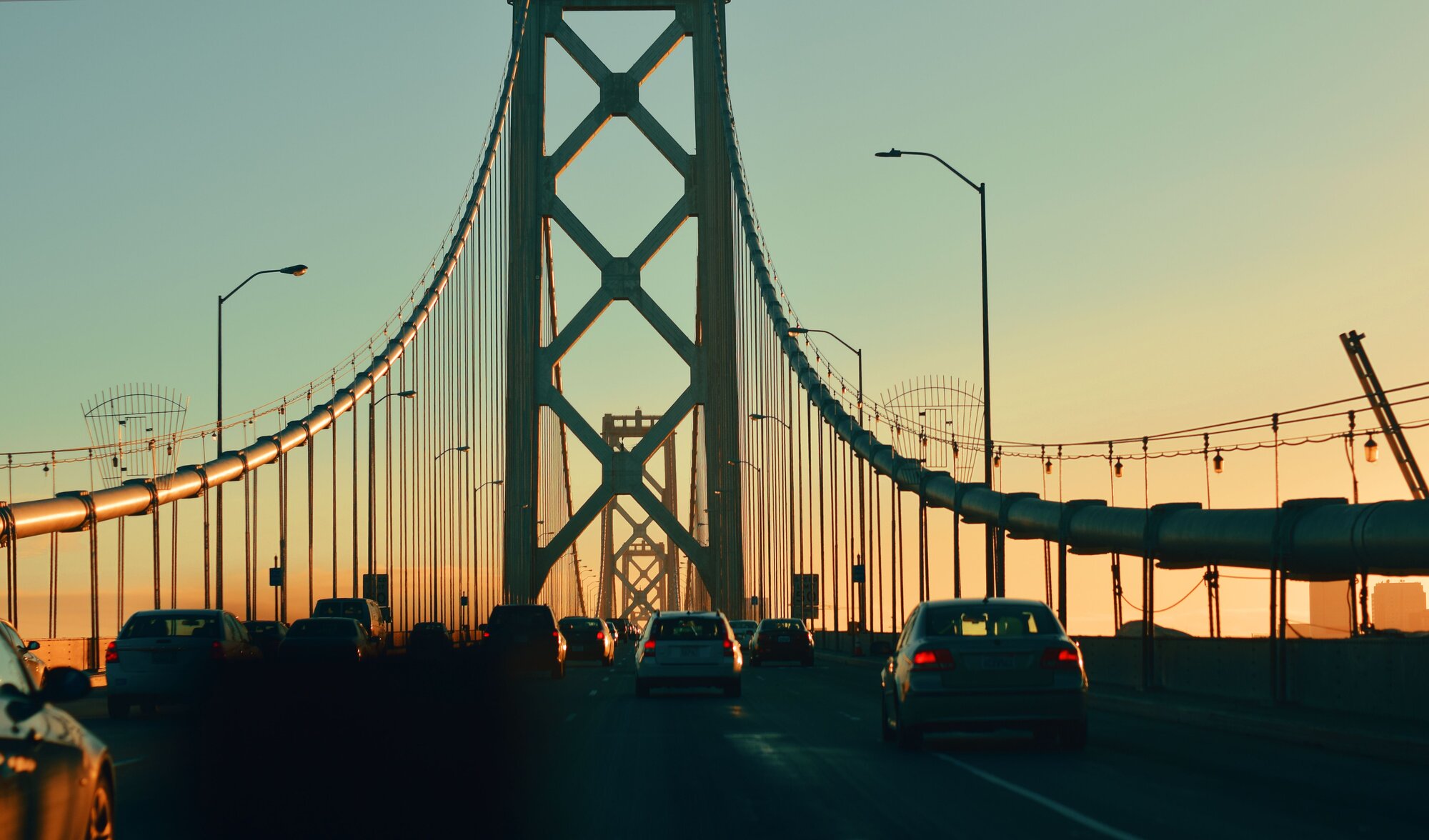 Vehicles on oakland bay bridge against sky at sunset