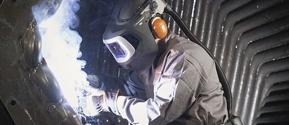 Man wearing a protective welding mask welds metal.