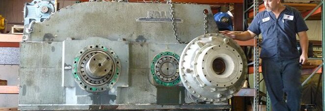 A Motion repair technician stands next to a large industrial gear box.