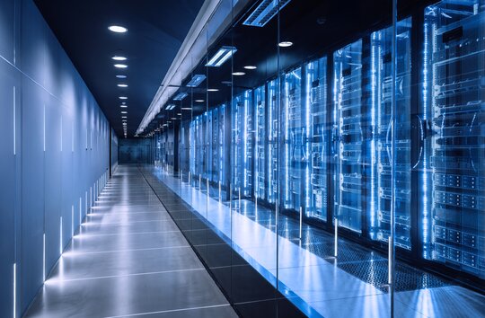 A row of servers line the wall of a large server room.