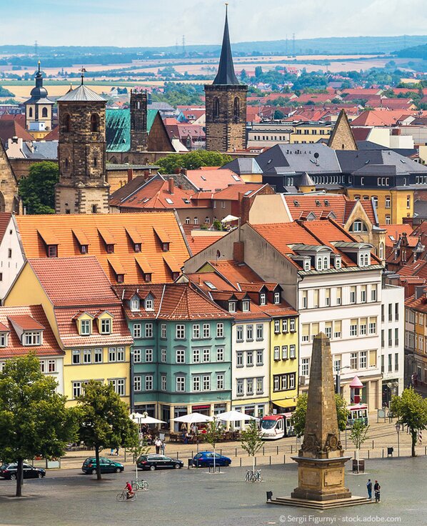 Offener Platz mit Denkmal in Erfurt. Im Hintergrund sieht man mehrere Kirchen und viele Dächer.