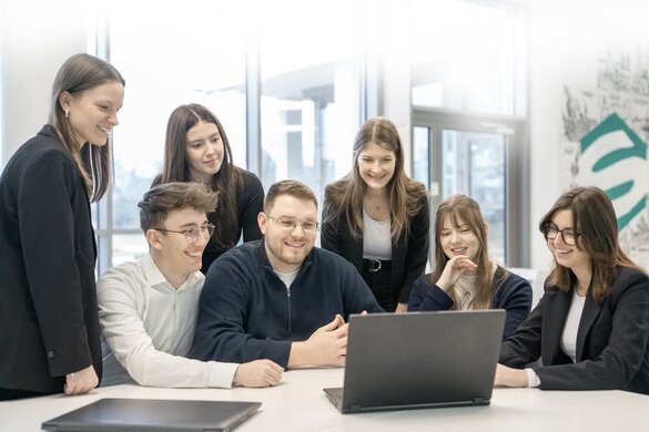 Gruppenfoto von Sellwerk Mitarbeitern die beim Standort Nürnberg die mit einem Laptop am Tisch sitzen und in die Kamera lächeln