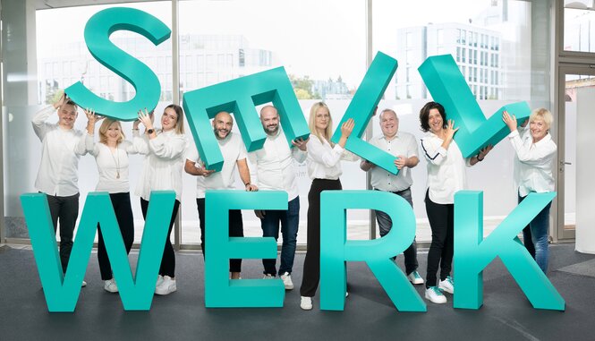 Ein Teamfoto der Werbeagentur SELLWERK, das alle Mitarbeiter zeigt, die entspannt und freundlich in die Kamera lächeln, umgeben von einer modernen und kreativen Büroatmosphäre.