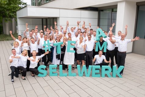 Team Sellwerk vom Standort Nürnberg mit dem Sellwerk Logo in der Hand