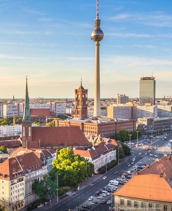 Fernsehturm in Berlin mit dem roten Rathaus und mehreren Dächern und einer Hauptstraße im Vordergrund. 