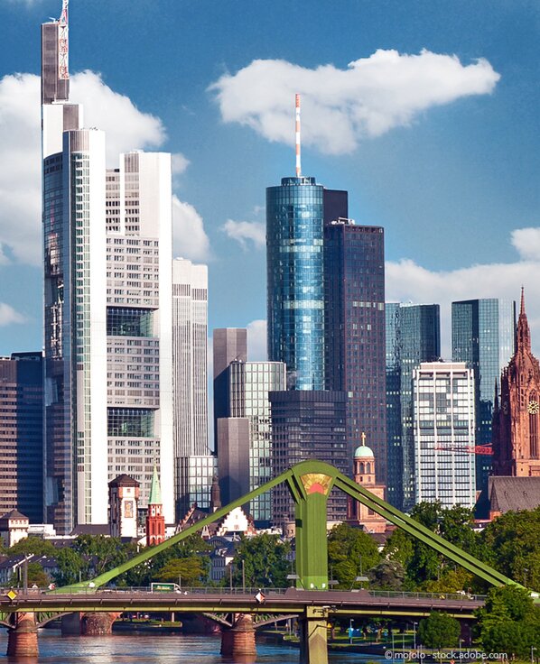 Skyline mit Wolkenkratzern in Frankfurt am Main. Vorne sieht man eine grüne Brücke.