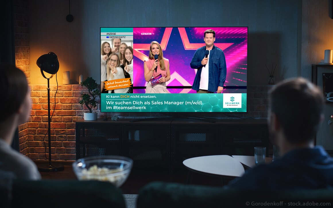 Foto in dem ein Pärchen vor dem Fernseher sitzt und das Supertalent auf RTL schaut. Im Bild wird ein Banner eingeblendet indem man ein Team SELLWERK Bild sieht und den Text Wir suchen Dich als Sales Manager (m/w/) im #teamsellwerk. 