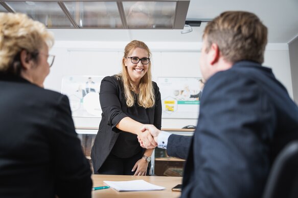 Ein SELLWERK Mitarbeiter schüttelt die Hand einer Kundin. Daneben sitzt eine weitere Frau mittleren Alters.