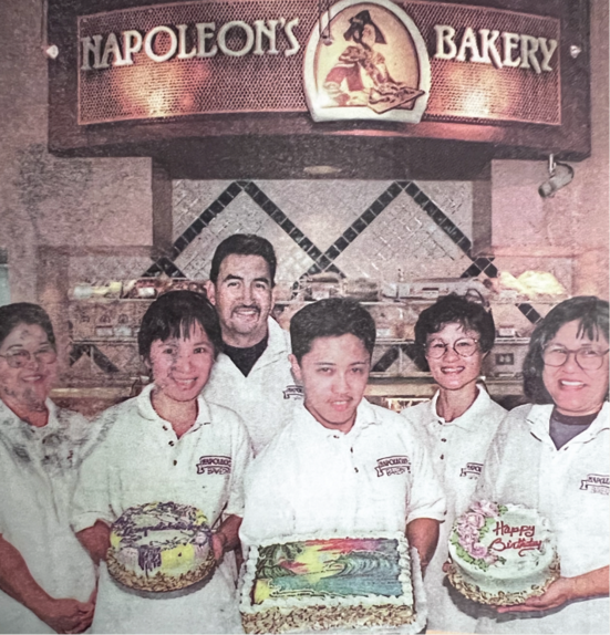 Napoleon's Bakery staff hold decorated cakes under the bakery sign