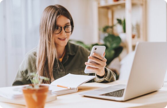 Female looking at her phone, with Laptop open and book in front of her