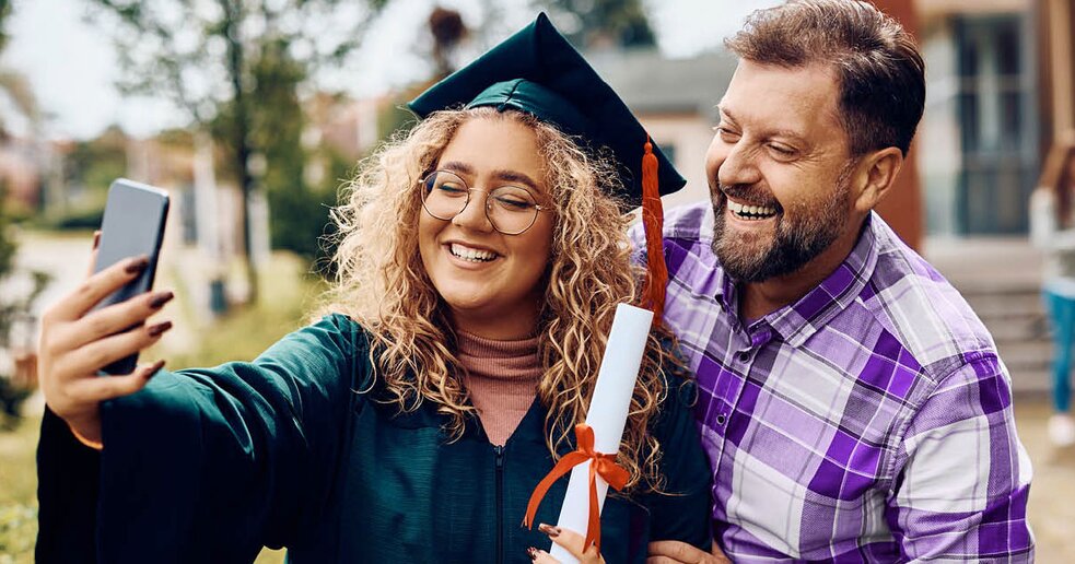A parent and a young adult child smiling in front of a college building, representing the use of home equity to fund higher education