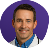 Headshot of Dr. Matt McGlasson wearing a white lab coat over a blue collared shirt, smiling, against a purple circular background.