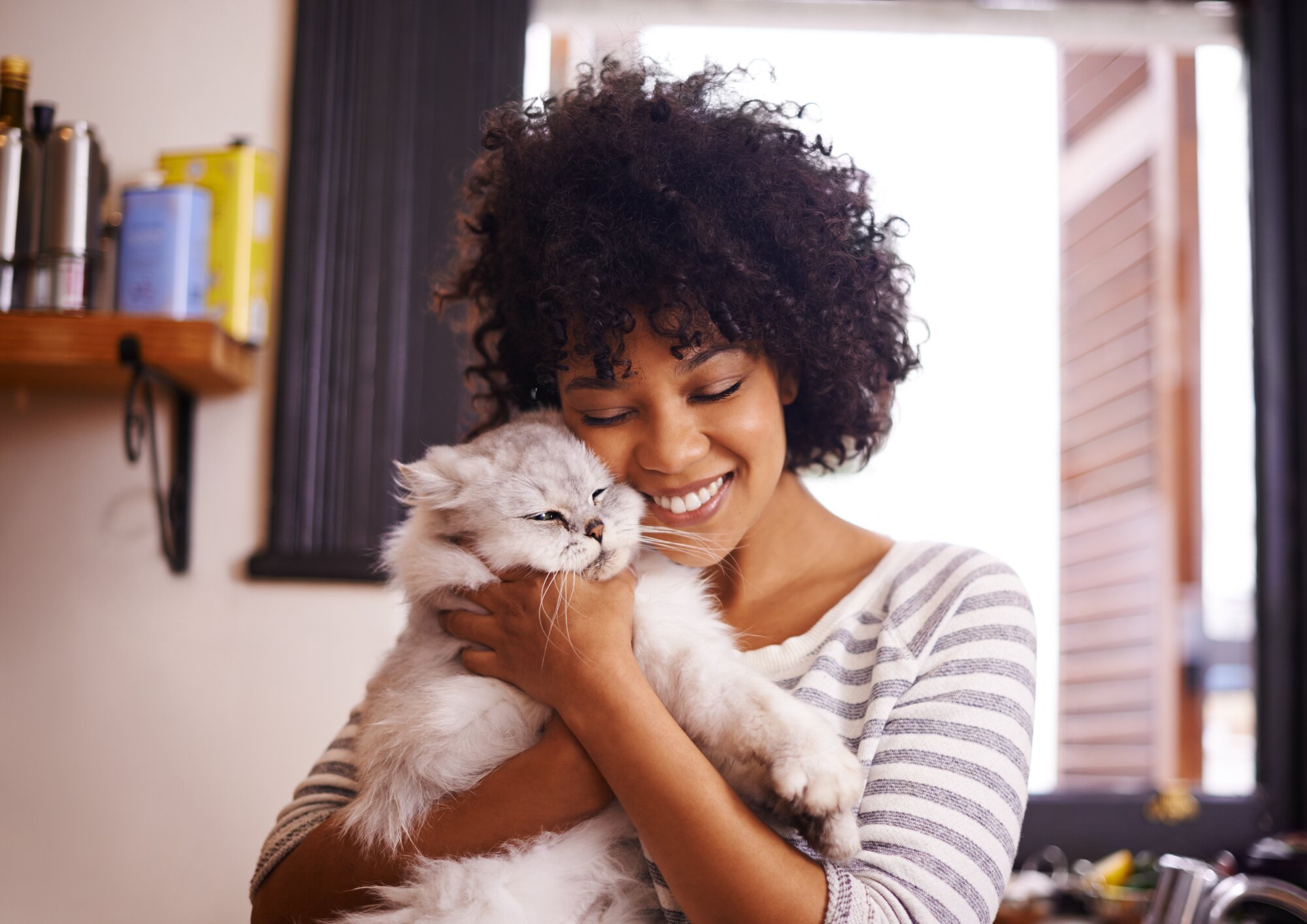 A young woman lovingly hugging her fluffy gray and white cat.