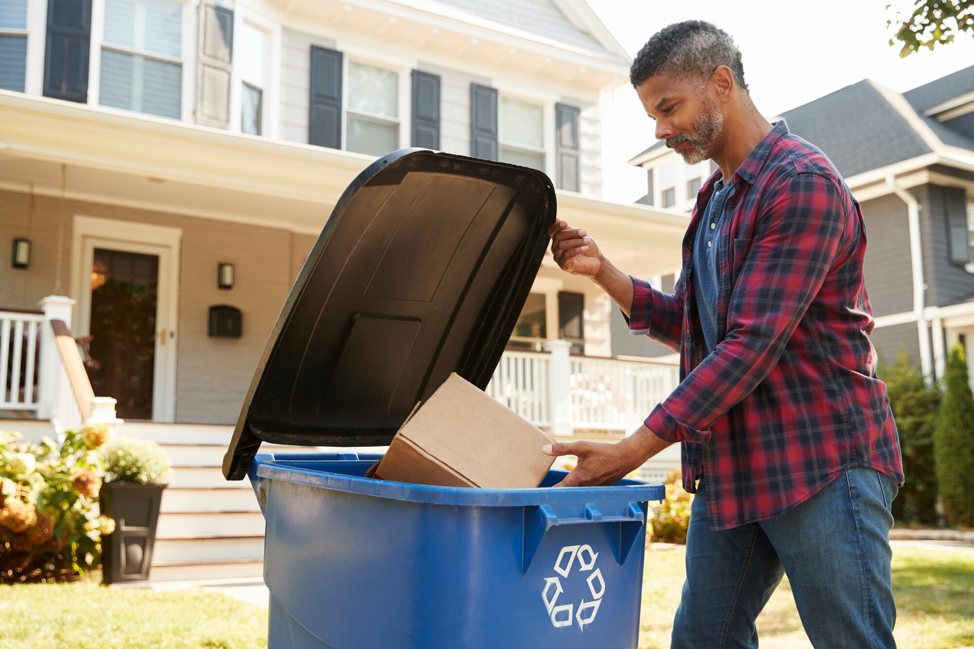 A man putting a cardboard box in a recycling bin outside