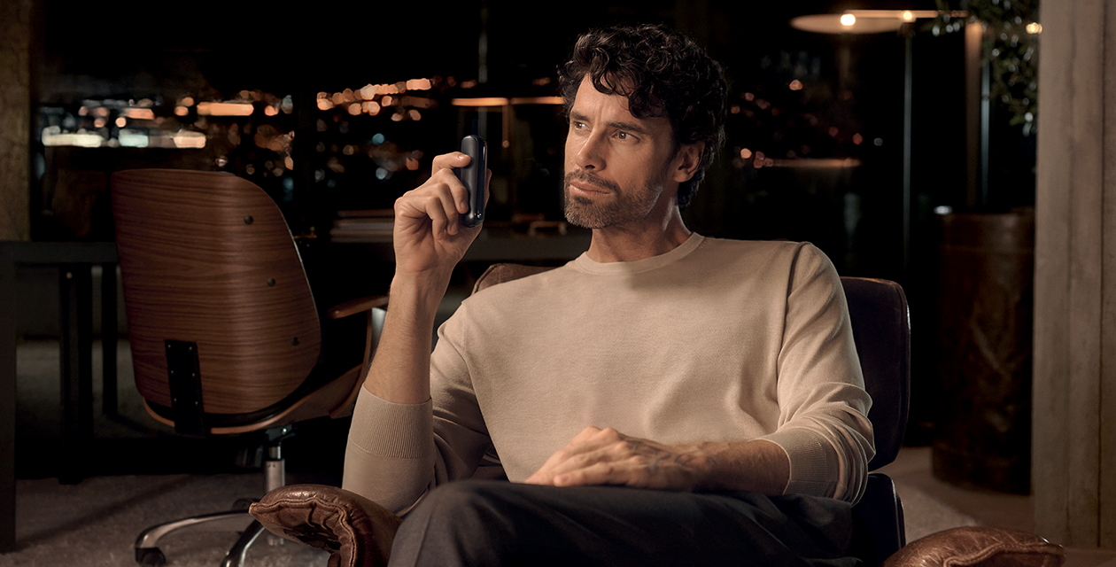 Giovane uomo con barba seduto su una poltrona mentre tiene in mano device Ploom