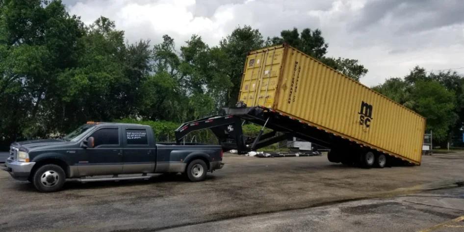 A shipping container being unloaded by a tilt-bed trailer