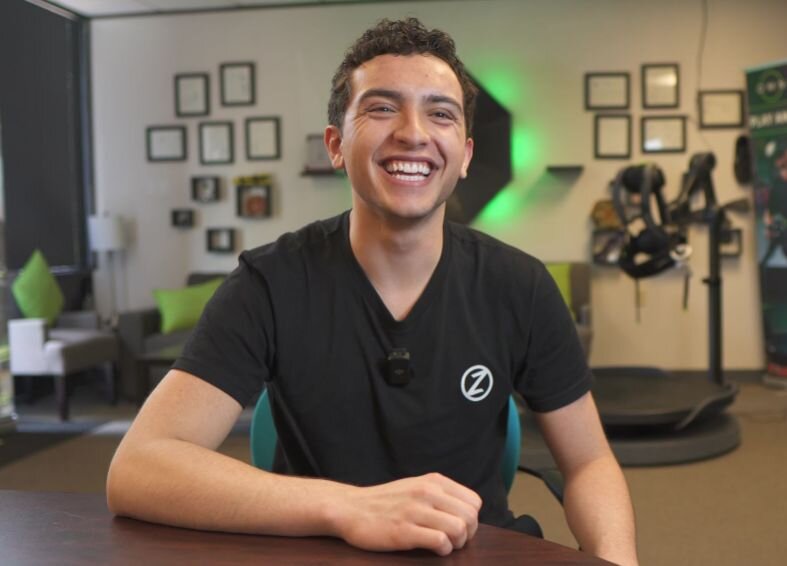 Content creator, Zulushi, is shown sitting at a table and smiling.