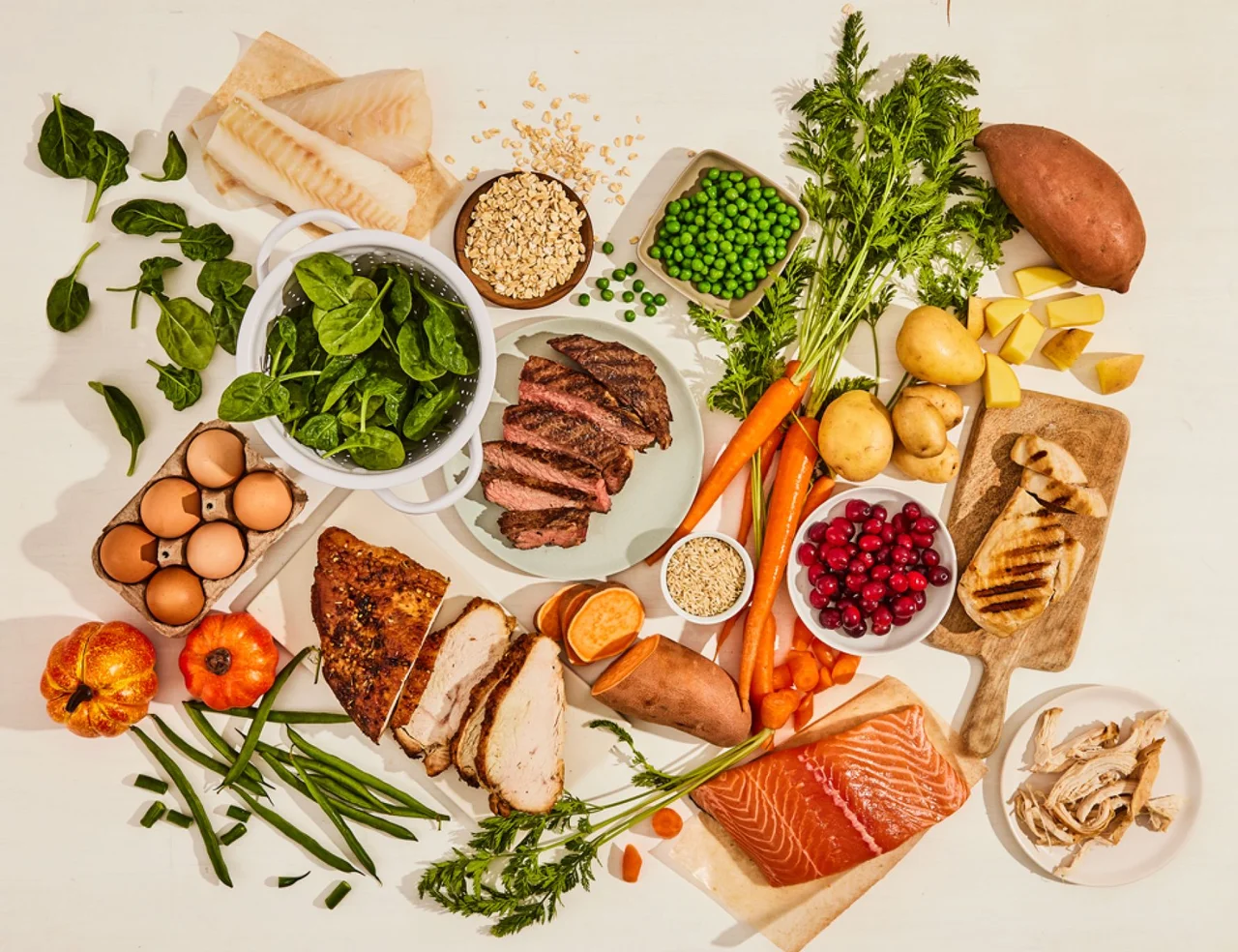 Overhead view of assorted fresh ingredients including meats, fish, eggs, vegetables, and grains.
