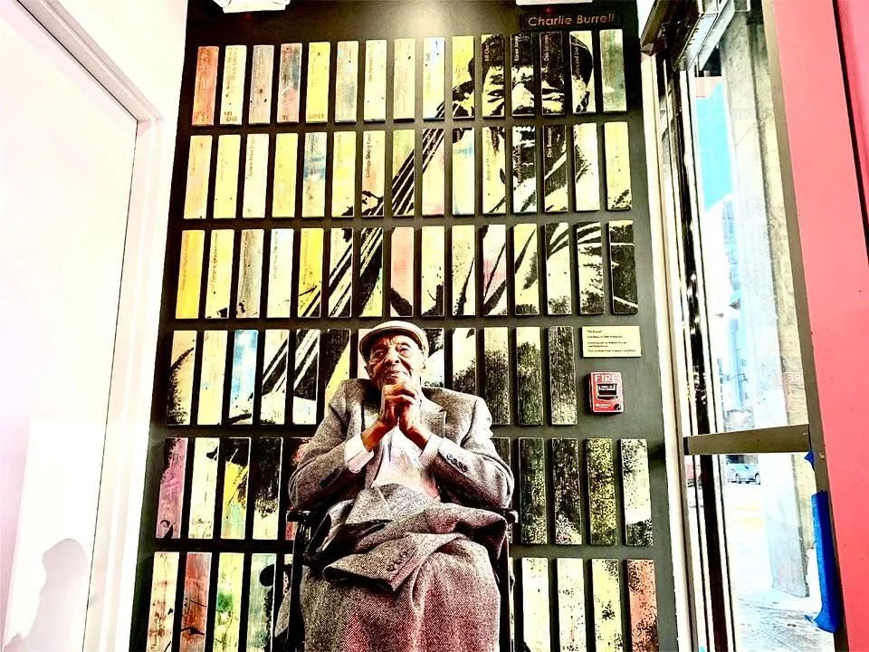 Charlie Burrell sitting in front of a mural of his likeness at Dazzle.