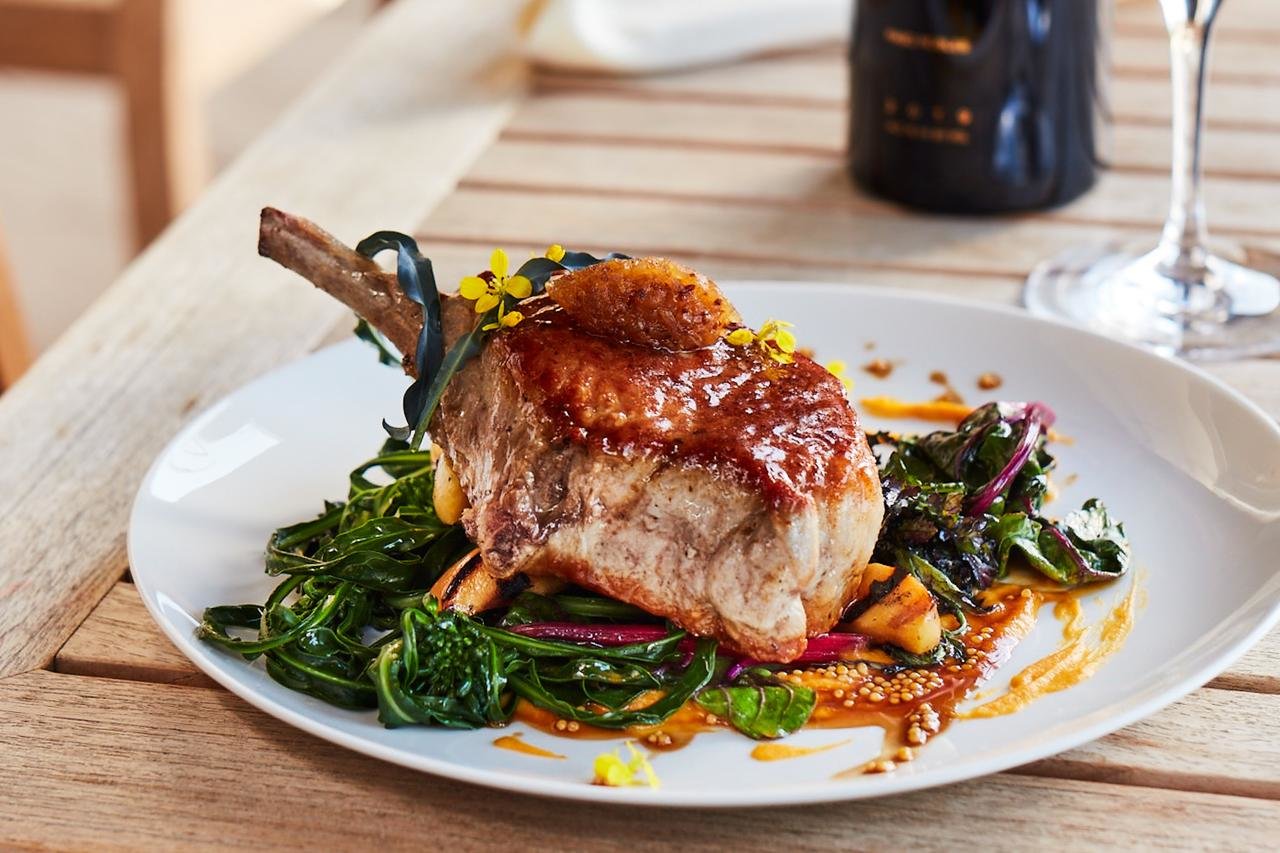 A thick porkchop with a golden, plum-colored crust and greens.