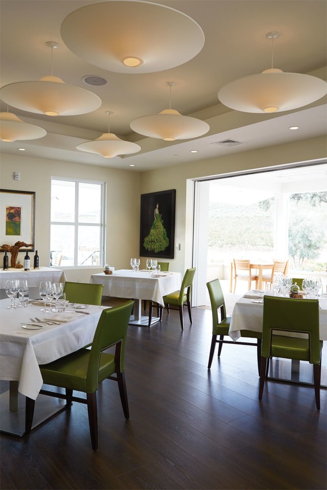 A bright, cream dining room with silky green chairs, trees outside the open patio doors. 