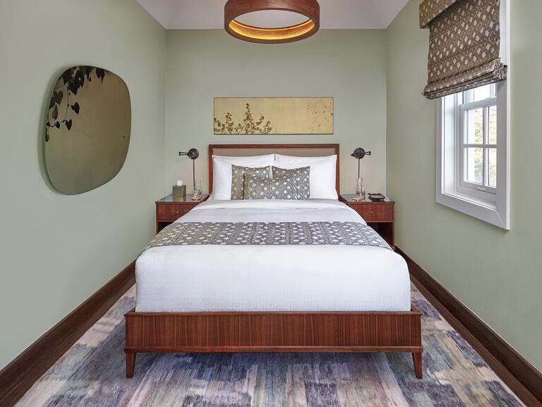 A bedroom with light mint green walls, a white bed, and a window on the right side. 