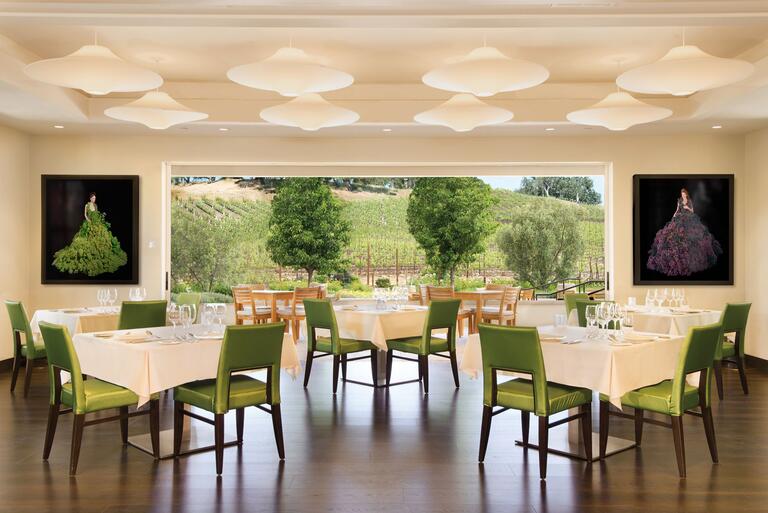 A smiling couple enjoys glasses of JUSTIN ISOSCELES and dessert in the patio shade,  the sunny vineyards behind them.