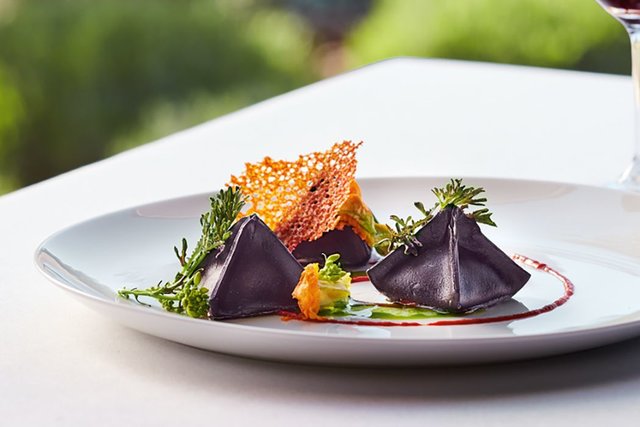 Dark purple, pyramid-shaped soppressini pasta with green garnish and a large crusted cheese crisp. 