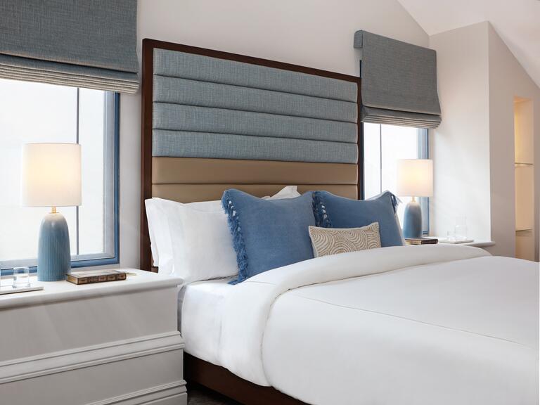 A bedroom with golden walls and luxurious red and brown fluffy bedding and matching curtains hanging over the bed. 