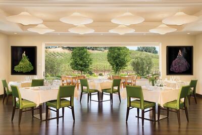 A bright, cream dining room with silky green chairs, trees outside the open patio doors.