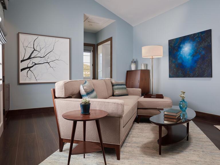 A living room with mint green walls and couch, midcentury wooden furniture, and two large art pieces on the walls.