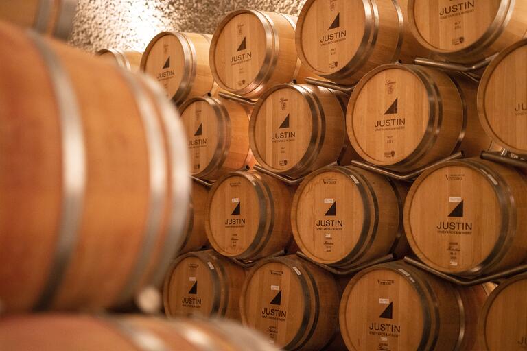 Black bottle necks protrude from a grid-like wine cellar wall, tan corks peppered throughout the dimly-lit rows.