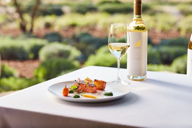 A bottle and glass of white wine and a plate of colorful salmon and vegetables.