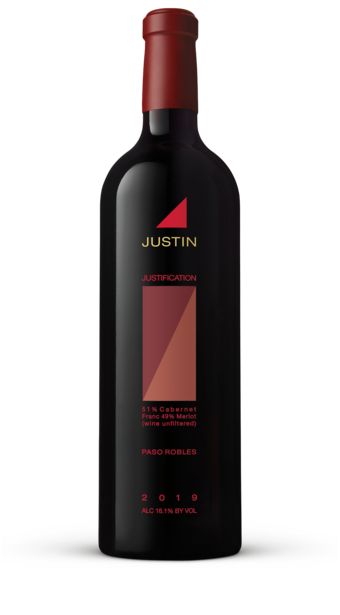 A bottle of JUSTIFICATION standing in front of a pink and purple sunset over the vineyard hills. 