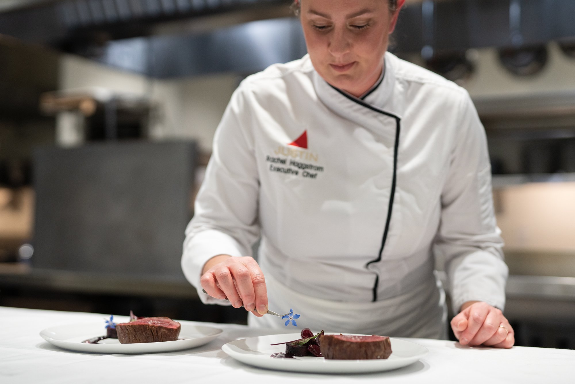 Executive Chef Rachel Haggstrom garnishes a beautifully pink, thick steak with a small, blue flower. 