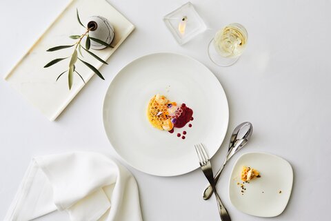  A white plate with a, elegant assortment of white truffles, pink sauce, and yellow honeycomb garnish. 