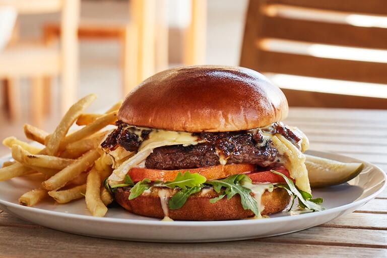 A juicy burger with cheese melting down the sides and a pile of fries next to it. 