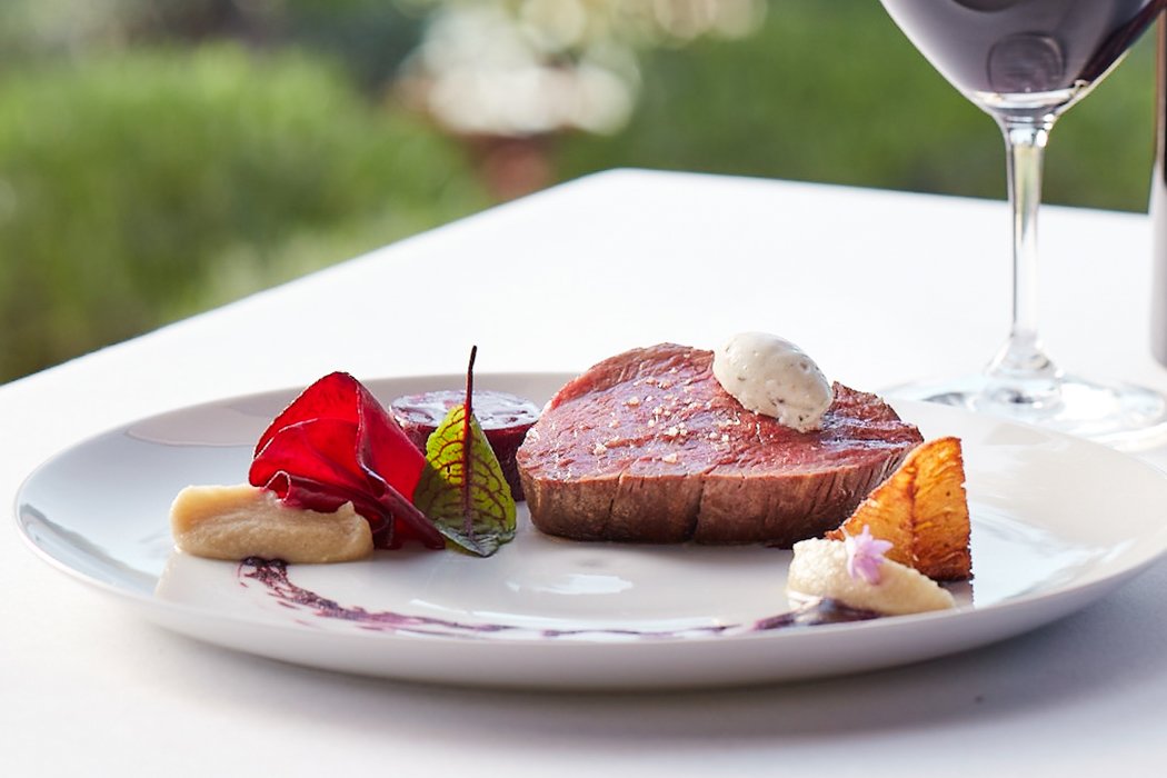 A thick, lean cut of filet mignon, topped with a butter quenelle and complemented by orange, red, and green garnishes. 