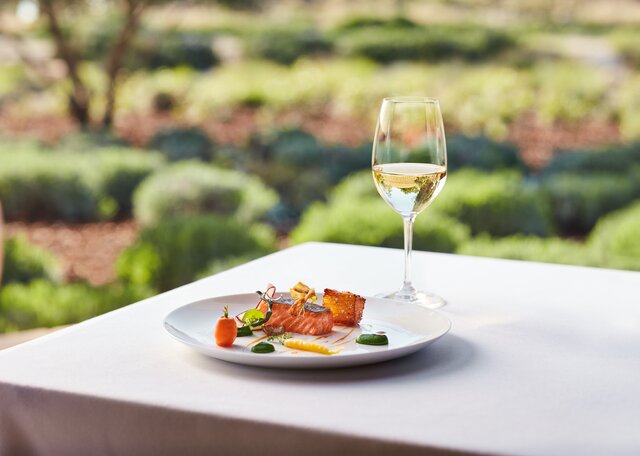 A bottle and glass of white wine and a plate of colorful salmon and vegetables.