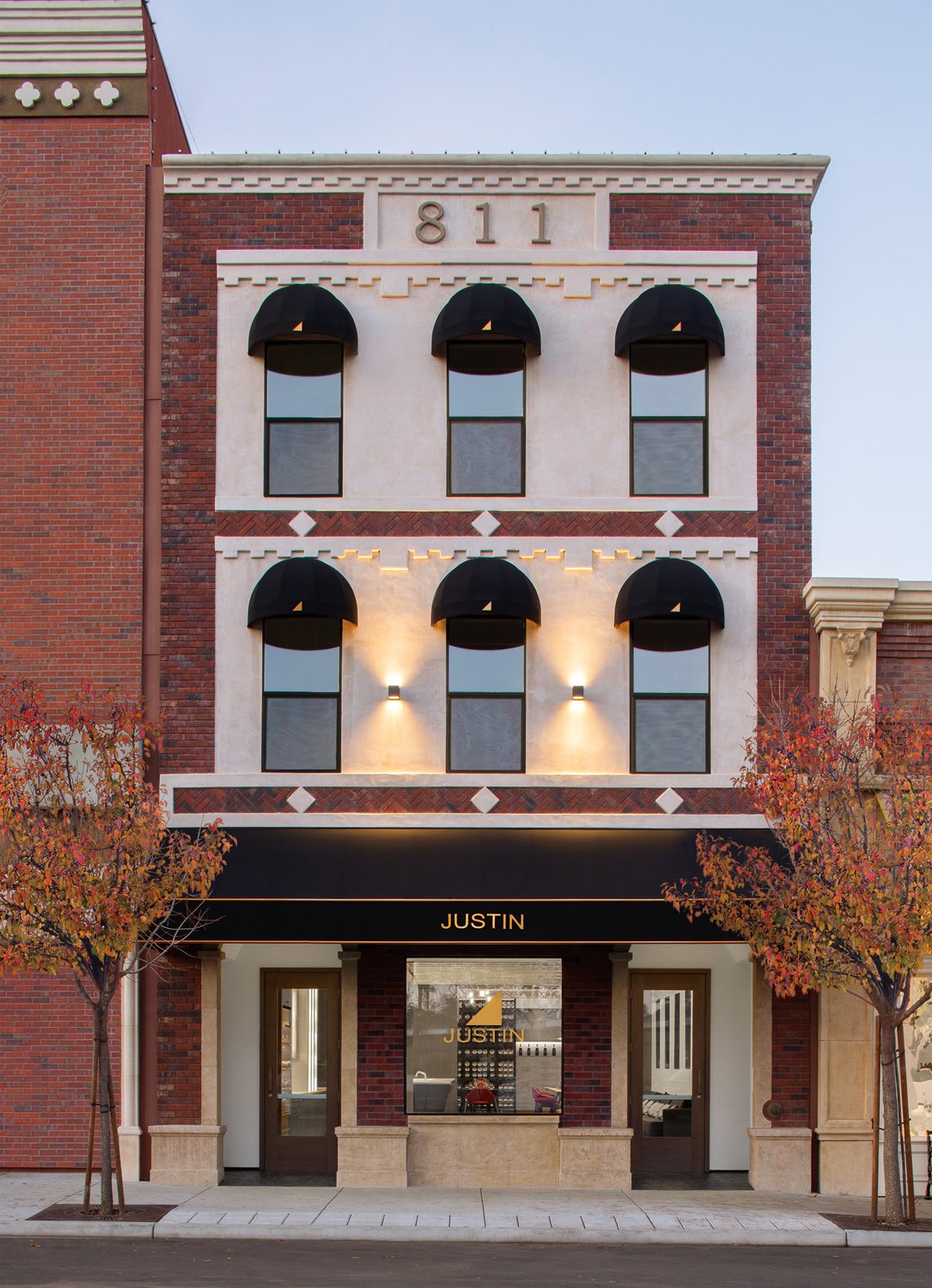 A narrow, three story, brick building with black domed awnings, the JUSTIN logo in gold on the largest window.
