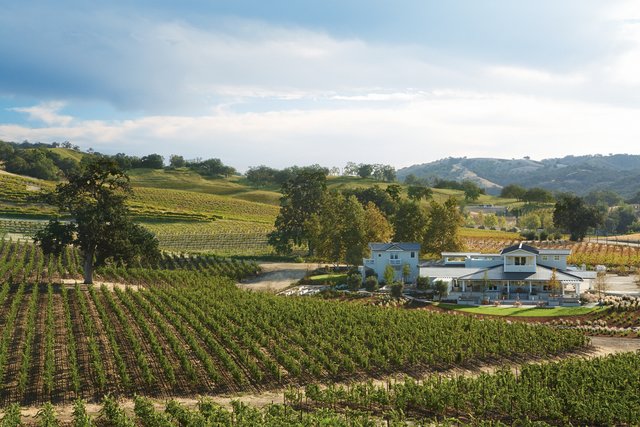 The rolling, green hills of the vineyard and a robin's egg blue sky surround the white, ranch style JUST Inn buildings. 